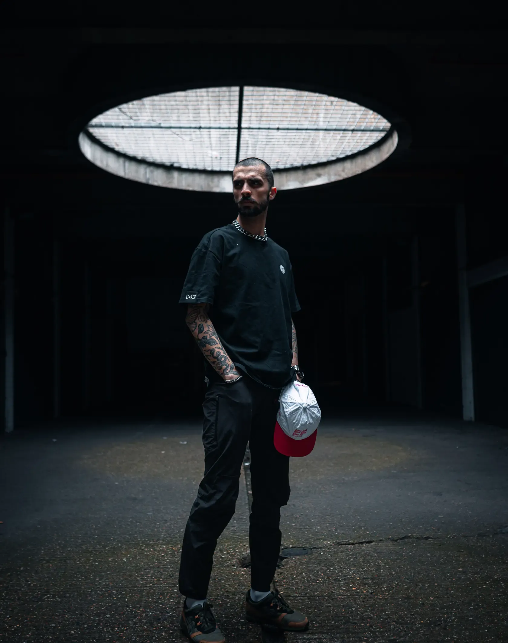 A photo of a man standing in an underground car park wearing the adaki T-shirt from the front