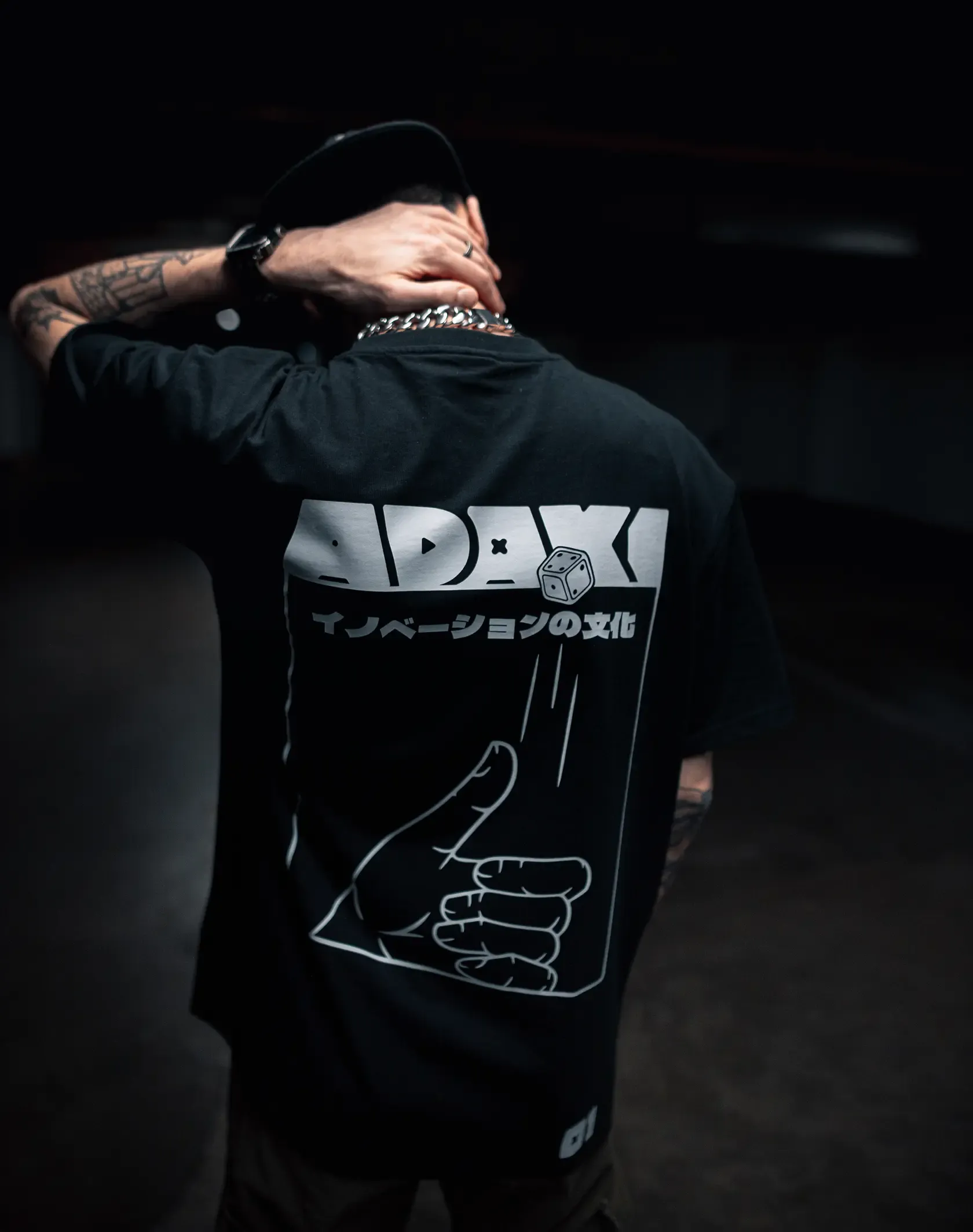 A close up photo of the back graphic on the Adaki T-shirt, being worn by a man with tattoos