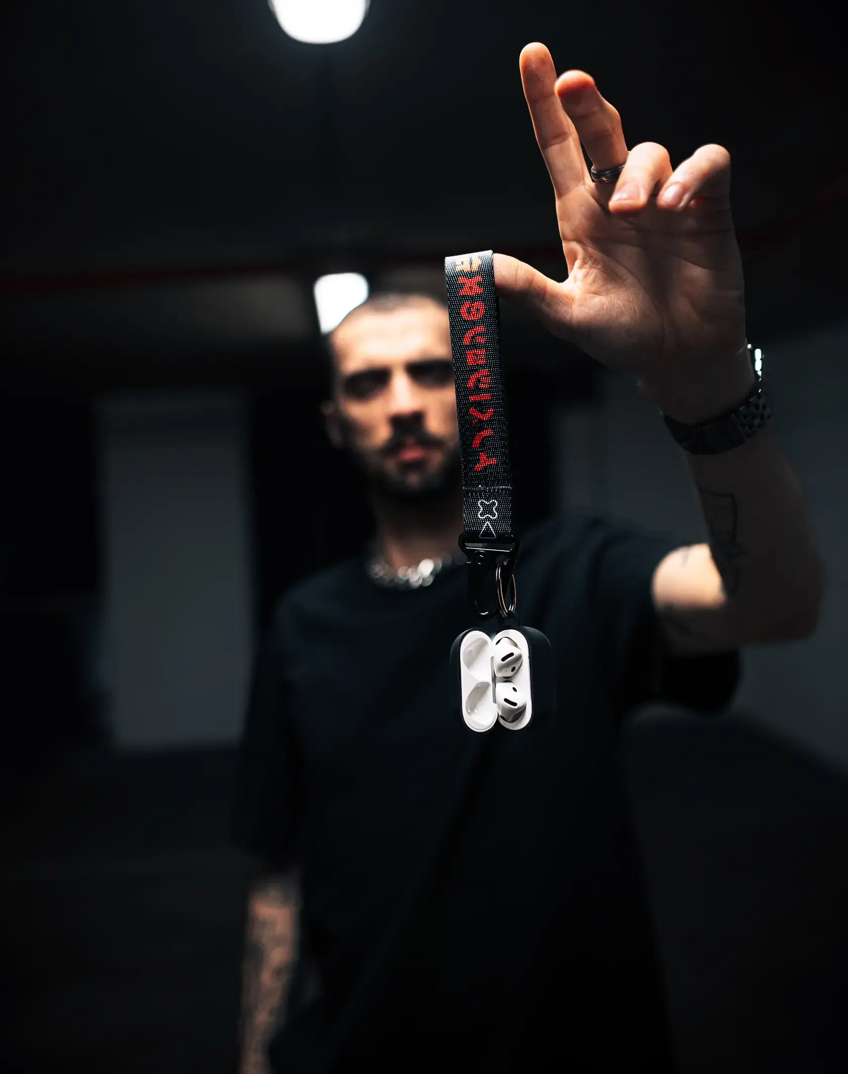 A close up photo of a man hanging the Adaki key chain off his finger that is attached to some AirPods
