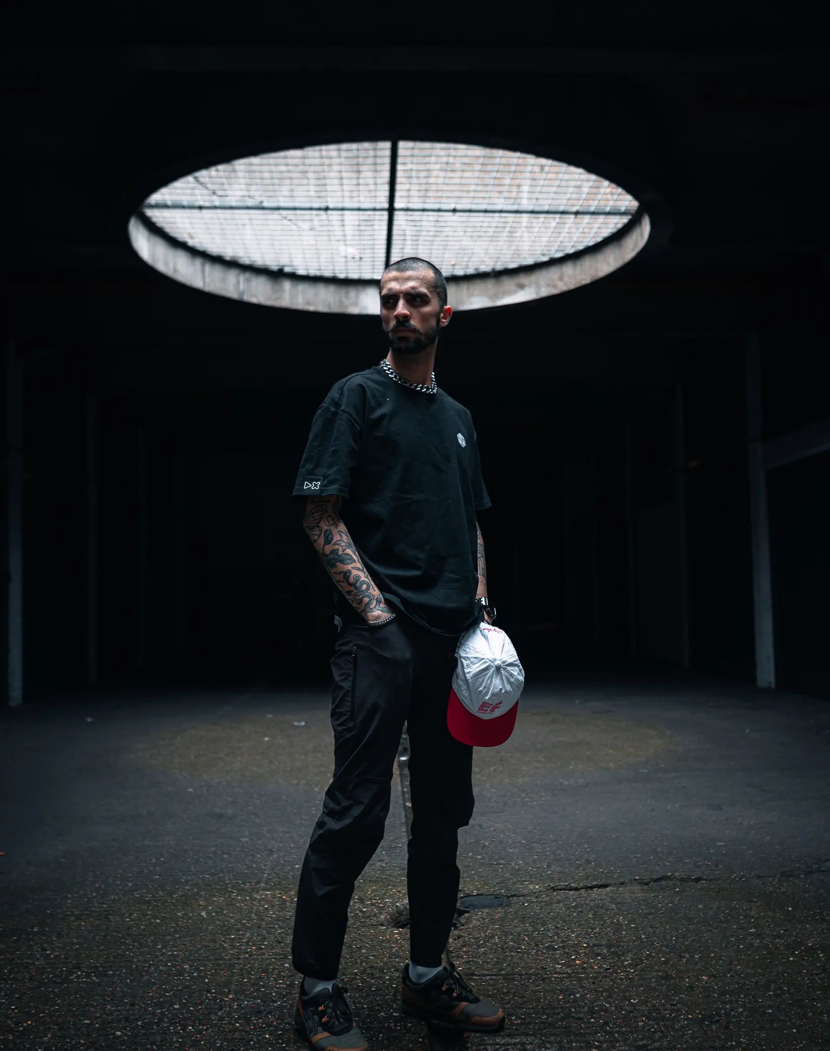 A photo of a man standing in an underground car park wearing the adaki T-shirt from the front