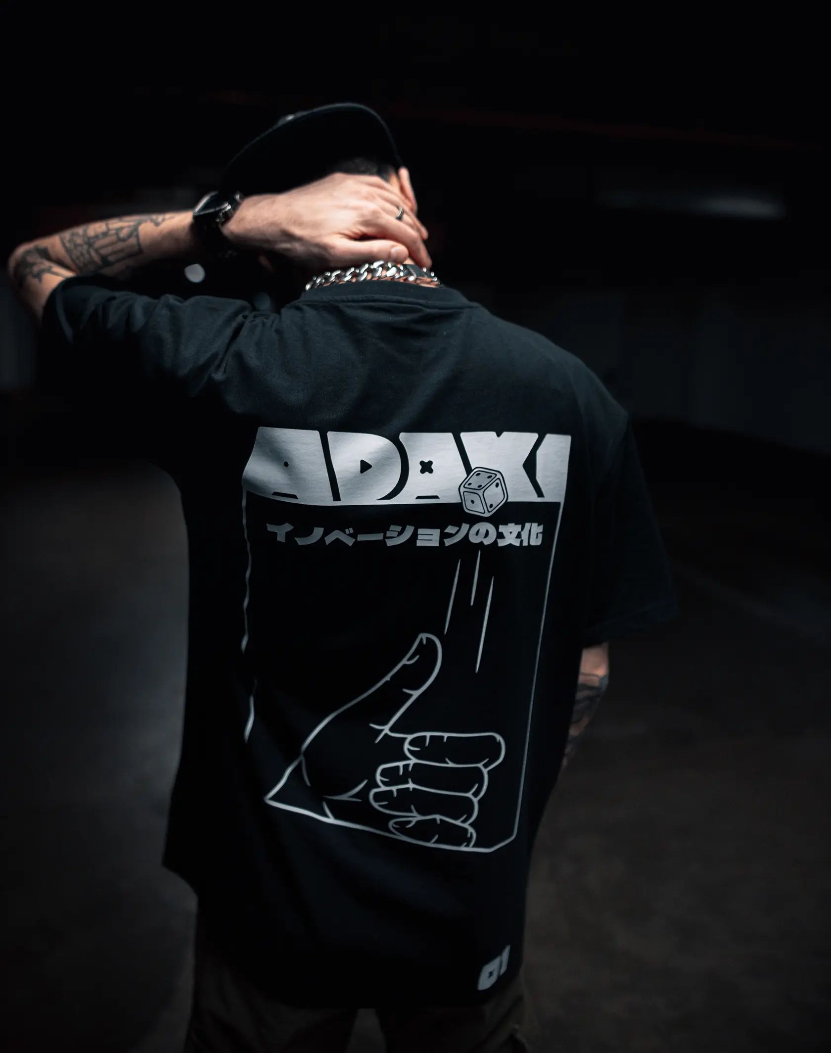 A close up photo of the back graphic on the Adaki T-shirt, being worn by a man with tattoos