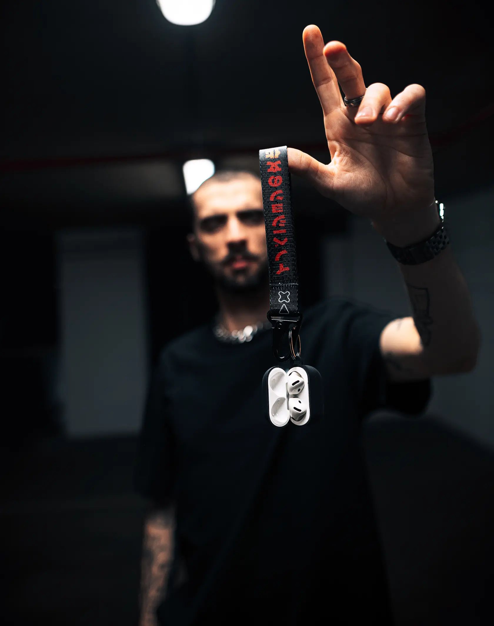 A close up photo of a man hanging the Adaki key chain off his finger that is attached to some AirPods